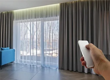 Hand using remote to open grey and sheer curtains