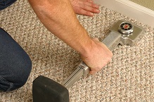 Installer stretching carpet using power stretcher tool