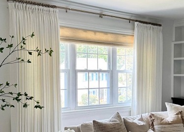 White pinch-pleat linen curtains on a brass rod beside a bright window